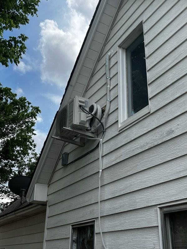 White house exterior with a window-mounted air conditioner unit and electrical conduit.