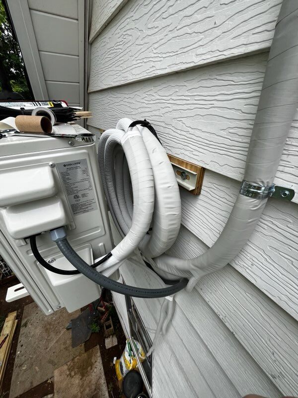 Exterior view of an air conditioner unit with insulated lines against white siding.