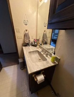 Bathroom sink with mirror, towel racks, and cabinet. Gray countertop.