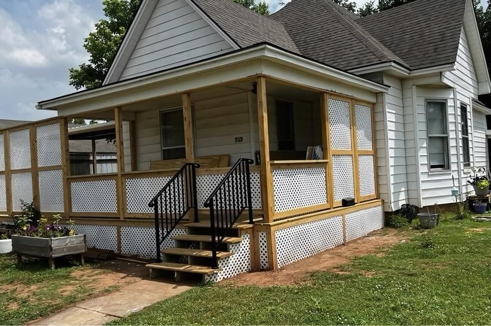 White house with a porch. Wooden steps and railings lead to the porch. Beige siding and corrugated plastic.