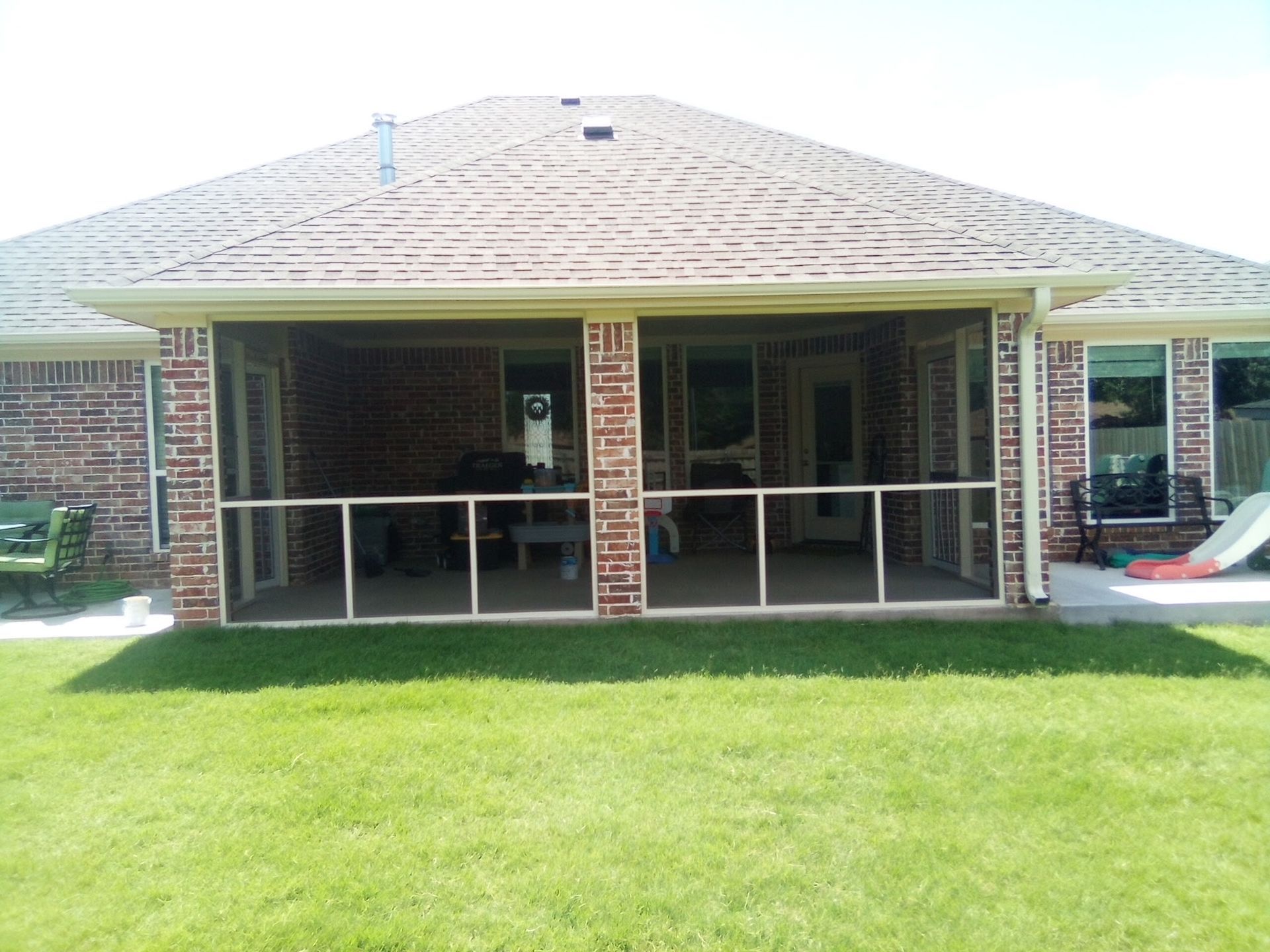 Screened-in patio attached to a brick house, with grass lawn in the foreground.