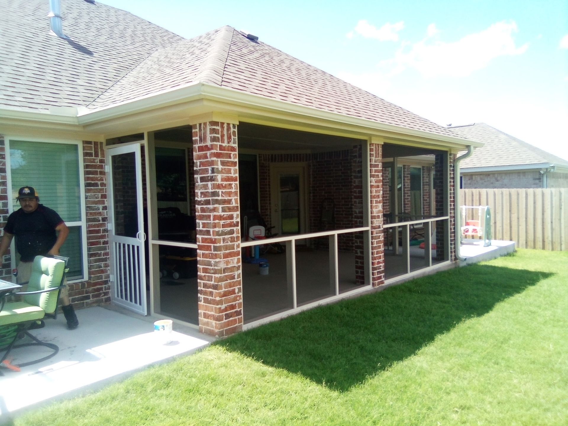 Screened porch with brick pillars, open to the yard. A person stands near a table, sunshine.