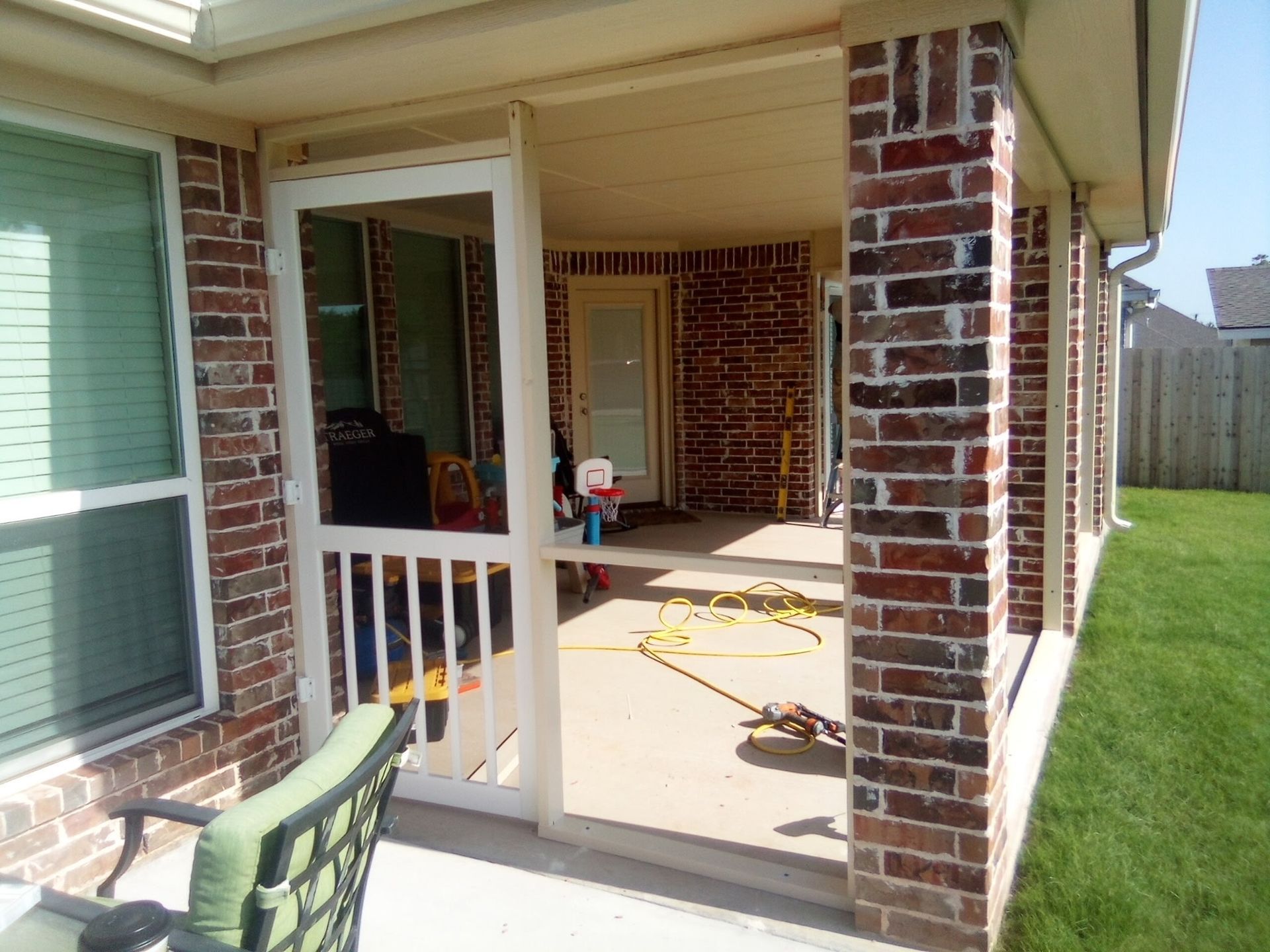 Brick-walled porch with screen door, concrete floor, and green lawn visible.