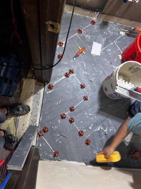 Person tiling a floor with gray tiles in a herringbone pattern, using spacers.