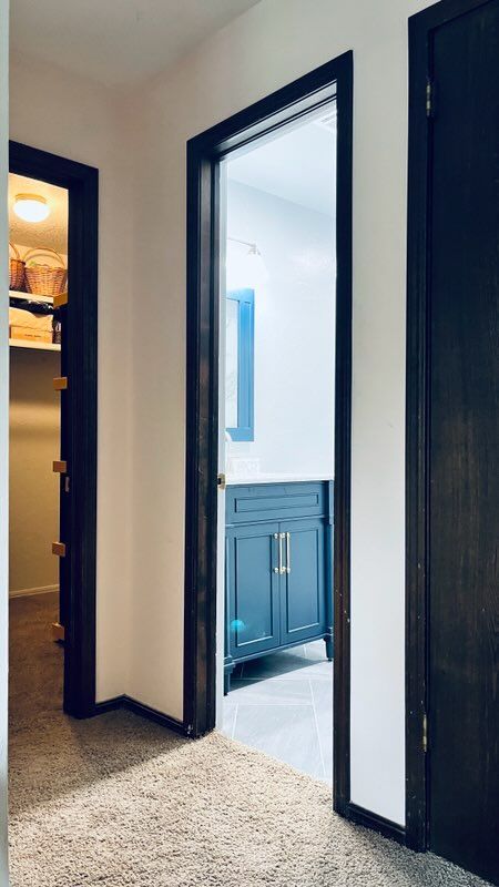 Hallway with dark-framed doors leading to a bathroom (blue vanity) and a closet with shelving.