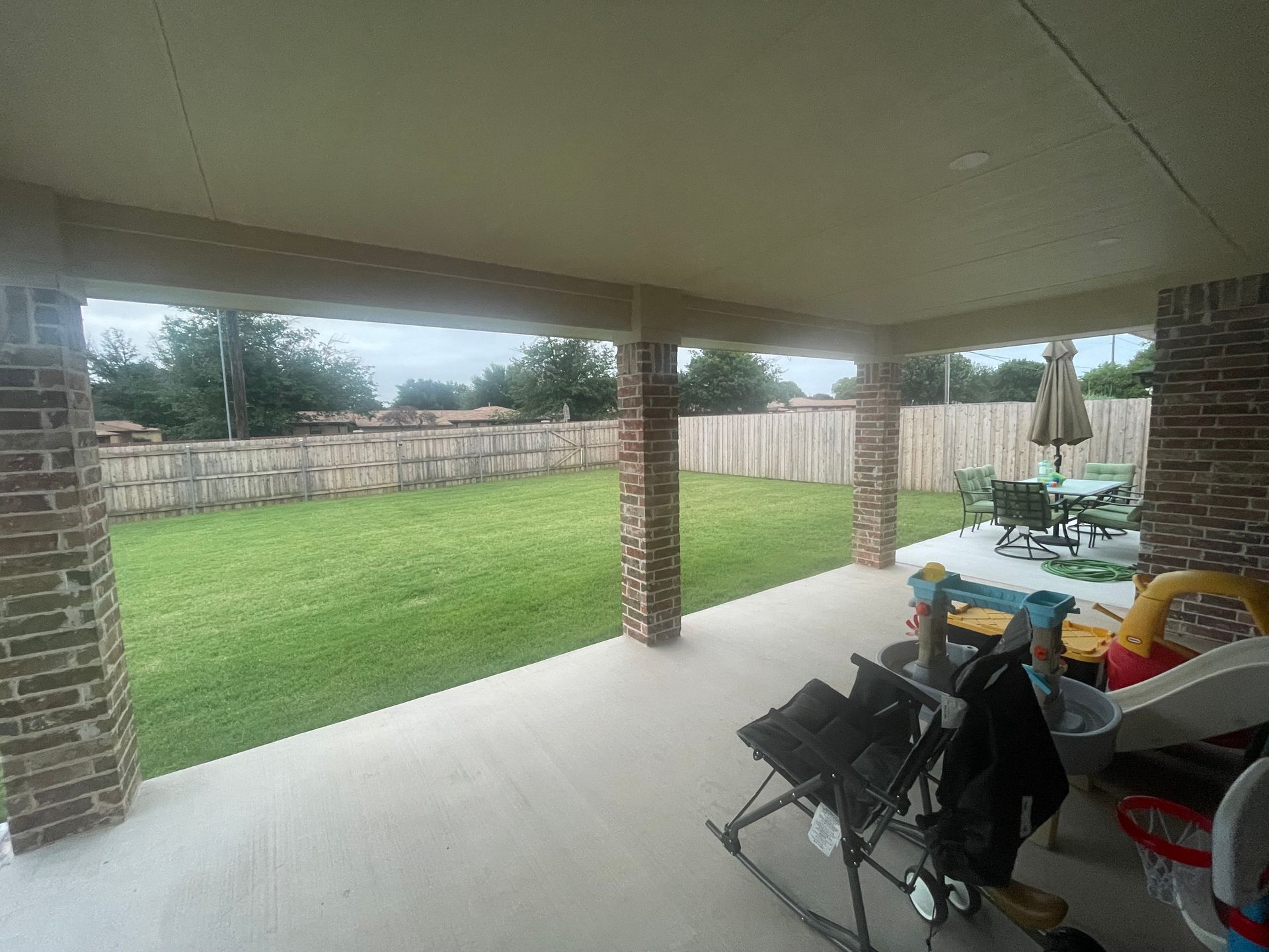 Covered patio overlooking a grassy yard, enclosed by a wooden fence.