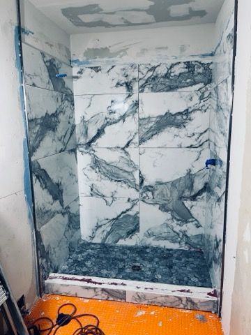 Shower stall with marble-patterned tiles, mosaic floor, and glass frame, under construction.