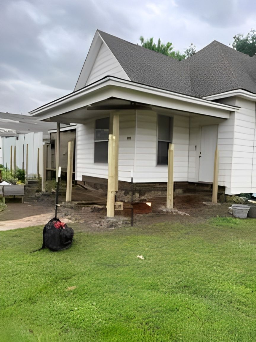 House with porch being remodeled; new support beams in place. Green grass, cloudy sky.