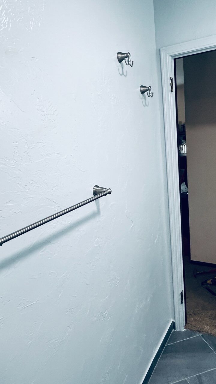 White bathroom wall with towel bar and two hooks, near a doorway.