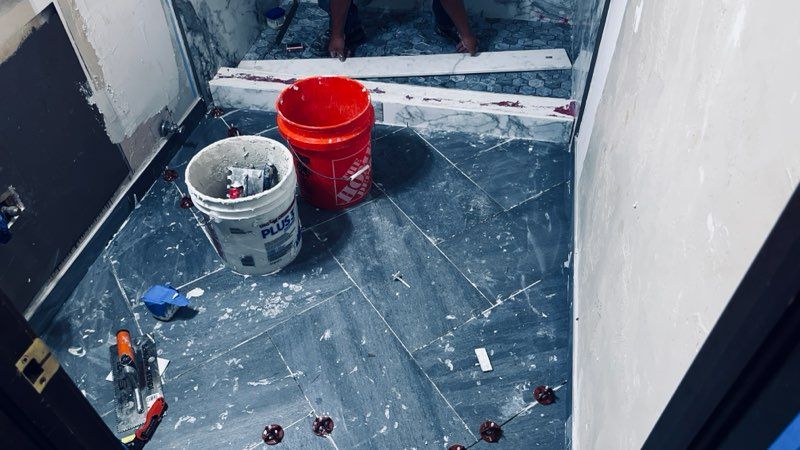 Bathroom floor tile installation in progress, tools and buckets on the floor, person in the background.