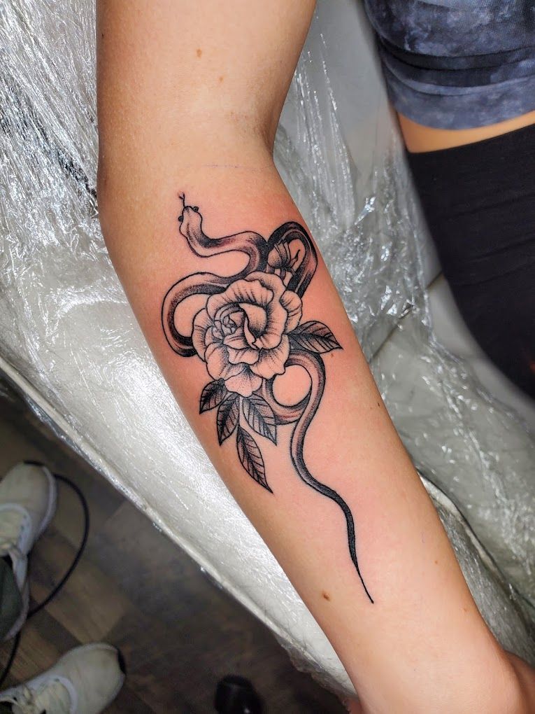 A woman has a tattoo of a snake and a rose on her arm.