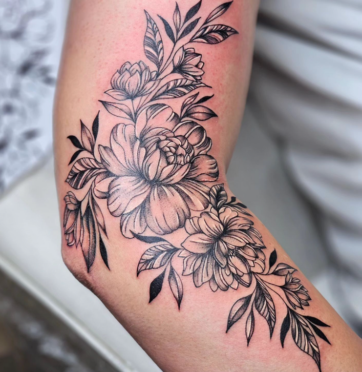 A woman has a tattoo of flowers and leaves on her arm.
