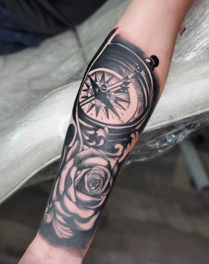 A person has a tattoo of a compass and roses on their forearm