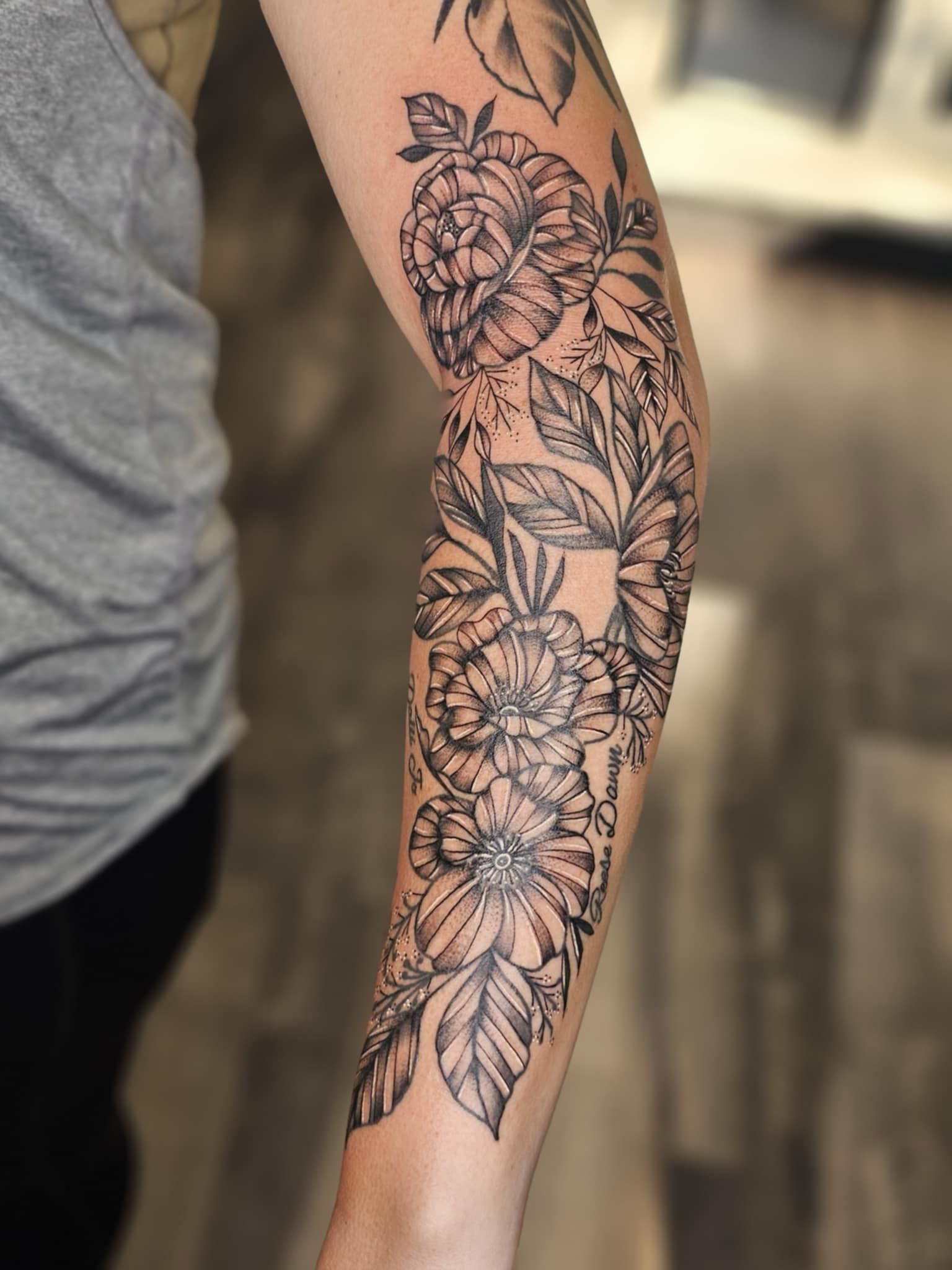 A woman has a tattoo of flowers and leaves on her arm.