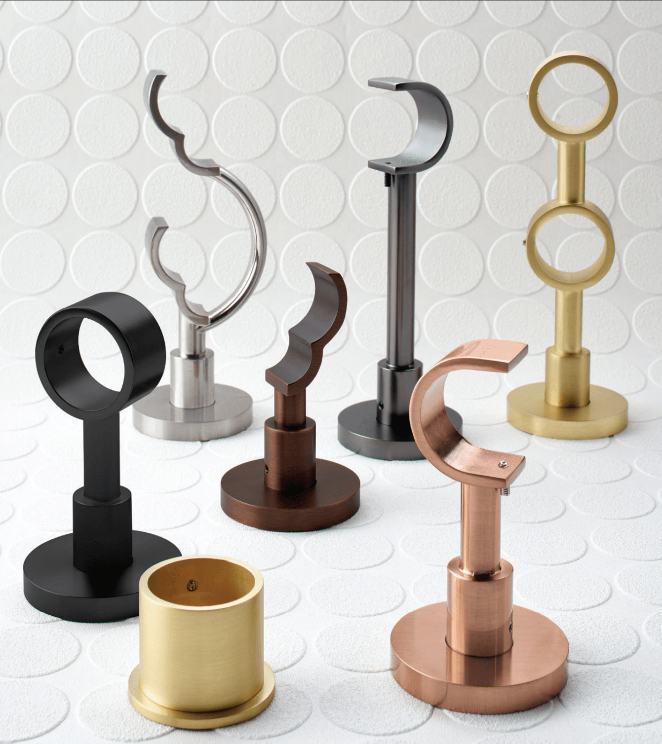 Assortment of metallic curtain rod holders in various shapes and finishes displayed against a white textured backdrop.