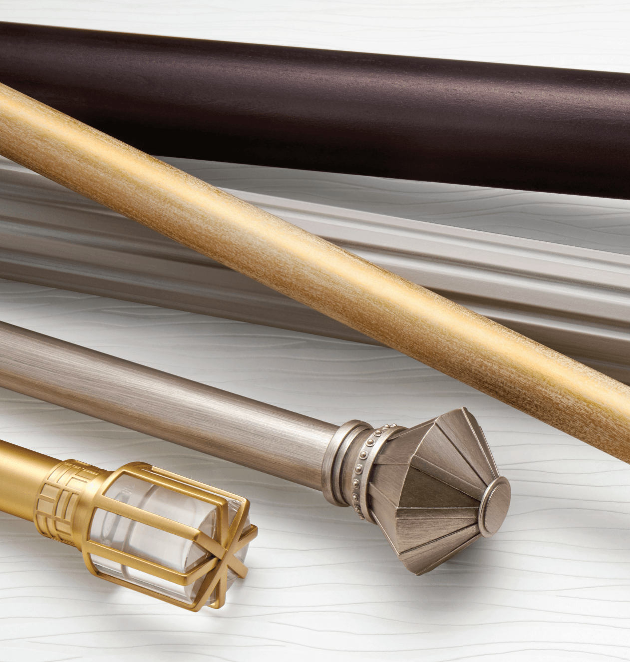 Close-up of different curtain rods in bronze, gold, and silver against a white background.