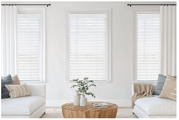 White living room with three windows, white sofas, and a wooden coffee table.