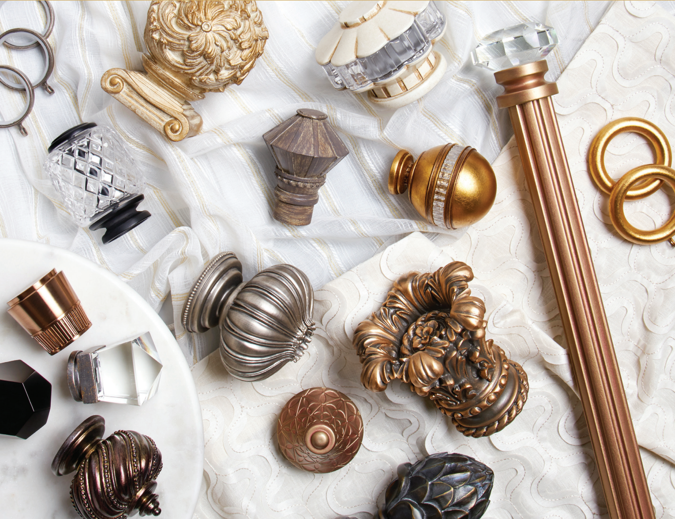 Variety of ornate curtain rod finials in gold, silver, and bronze on a white fabric background.