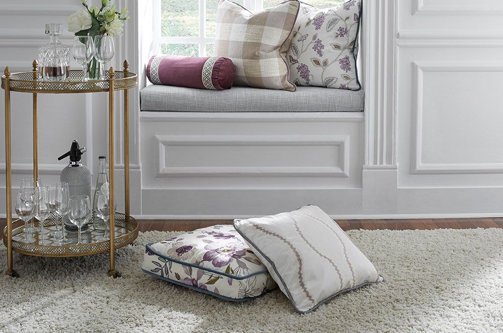 Window seat with pillows, gold bar cart, and white rug.