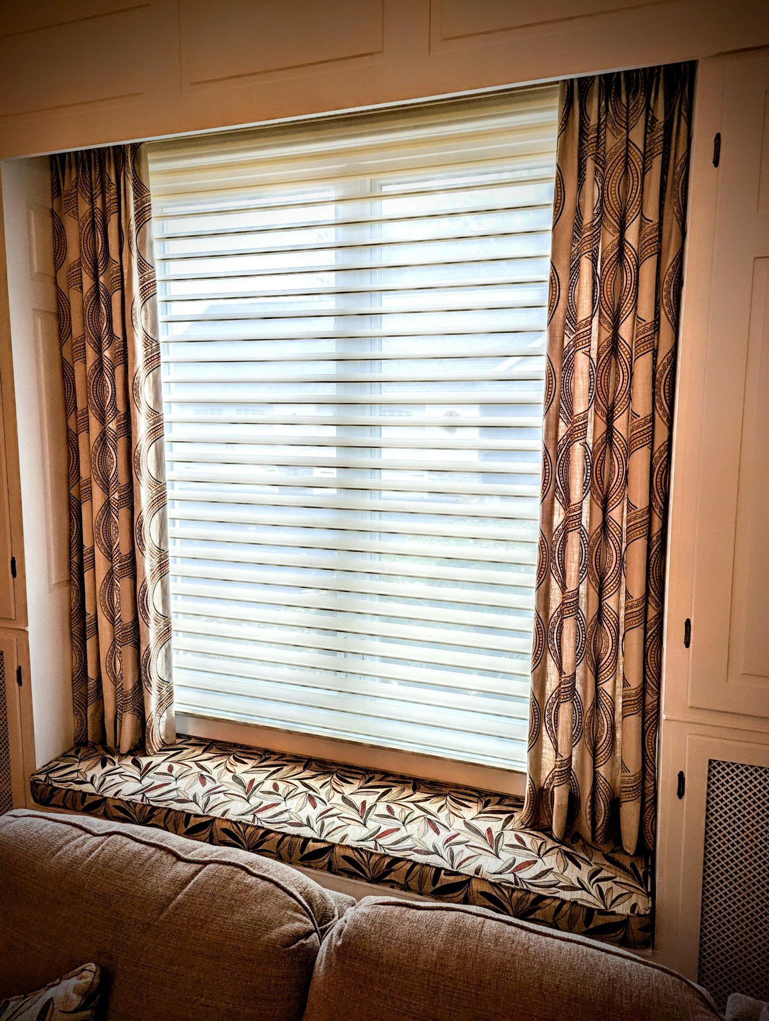Window with patterned curtains and a window seat above a sofa.