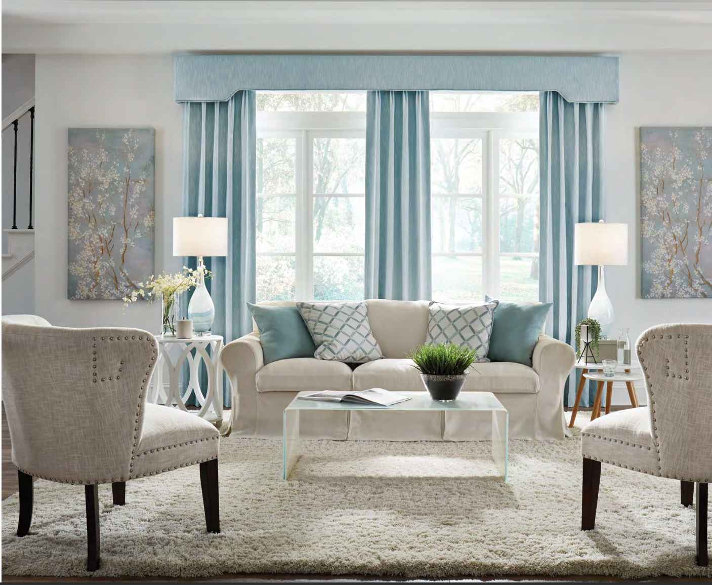 Living room with light blue accents, beige sofa, chairs, and rug. Window with curtains, artwork, lamps.