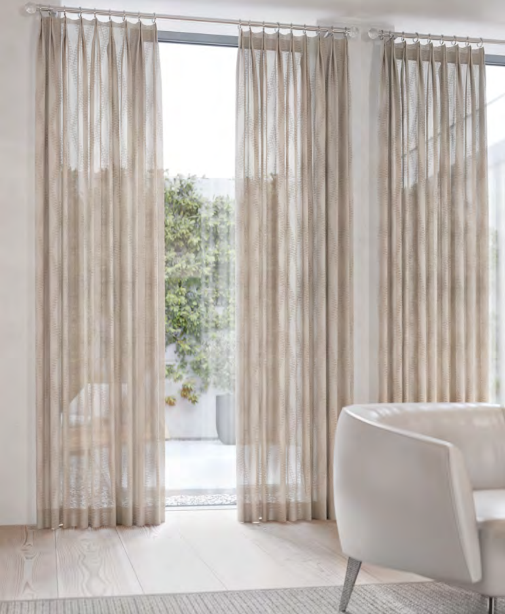Sheer beige curtains framing a bright window with a glimpse of greenery. A white chair sits nearby.
