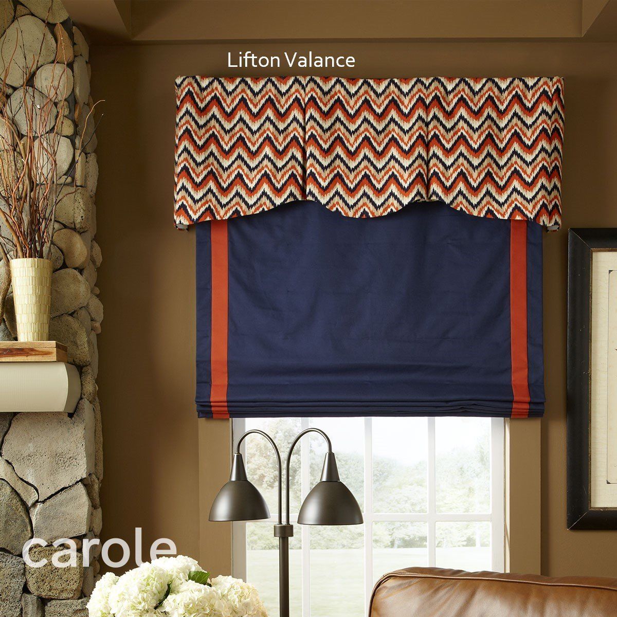Blue Roman shade with orange trim, under a patterned valance, over a window. Brown wall setting.
