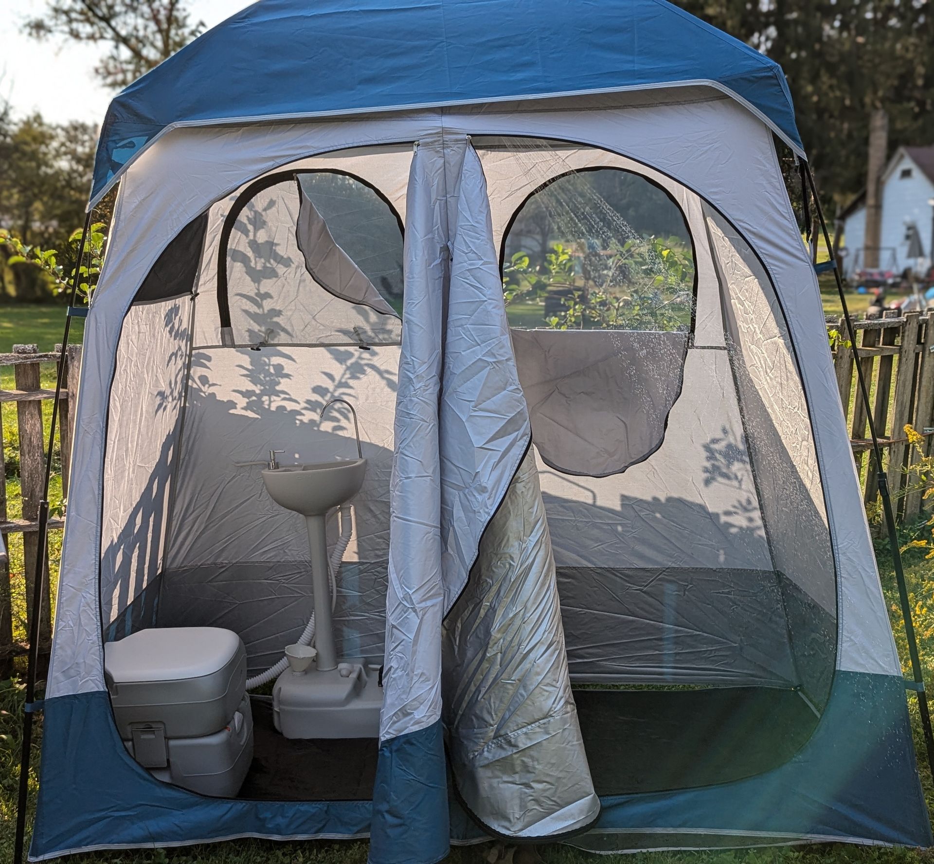 A portable camping shower and toilet inside an open, blue and gray tent outdoors.