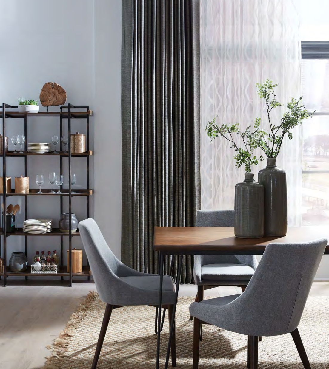 Dining room with gray chairs, wooden table, shelves, and window with patterned curtains.