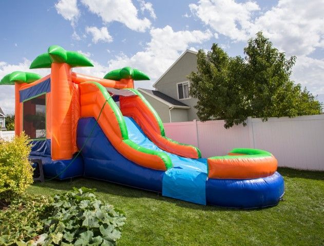 Colorful inflatable bounce house and slide in a backyard with green lawn and trees