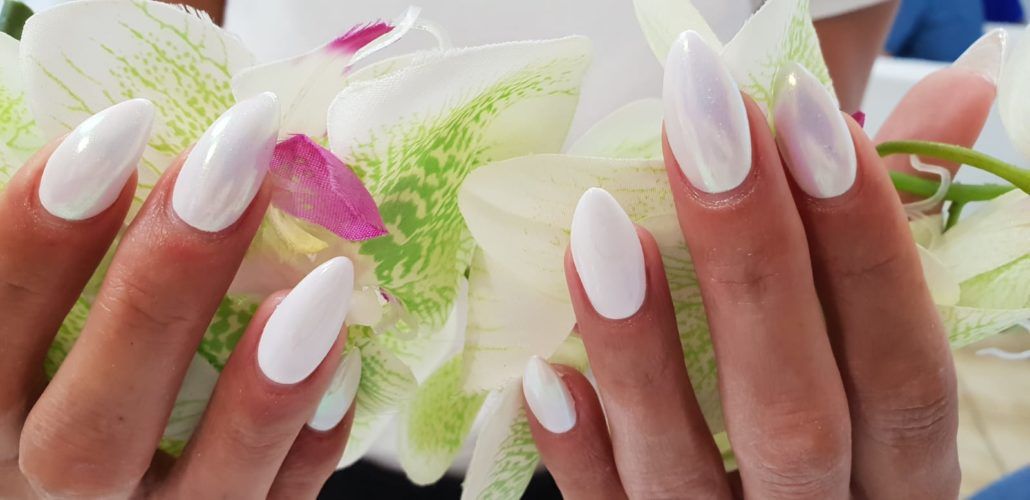 Eine Nahaufnahme der Hände einer Frau mit weißen Nägeln, die eine Blume halten.