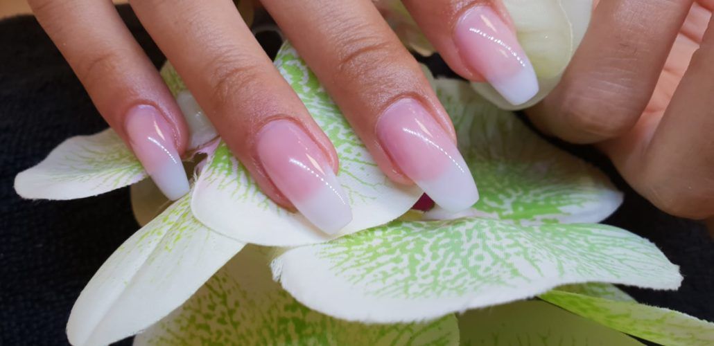 Eine Nahaufnahme der Nägel einer Frau mit einer Blume im Hintergrund.