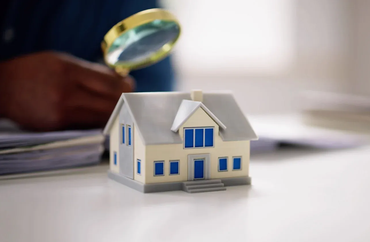 Two-story beige house with a green lawn and driveway. It has a bay window and a two-car garage.