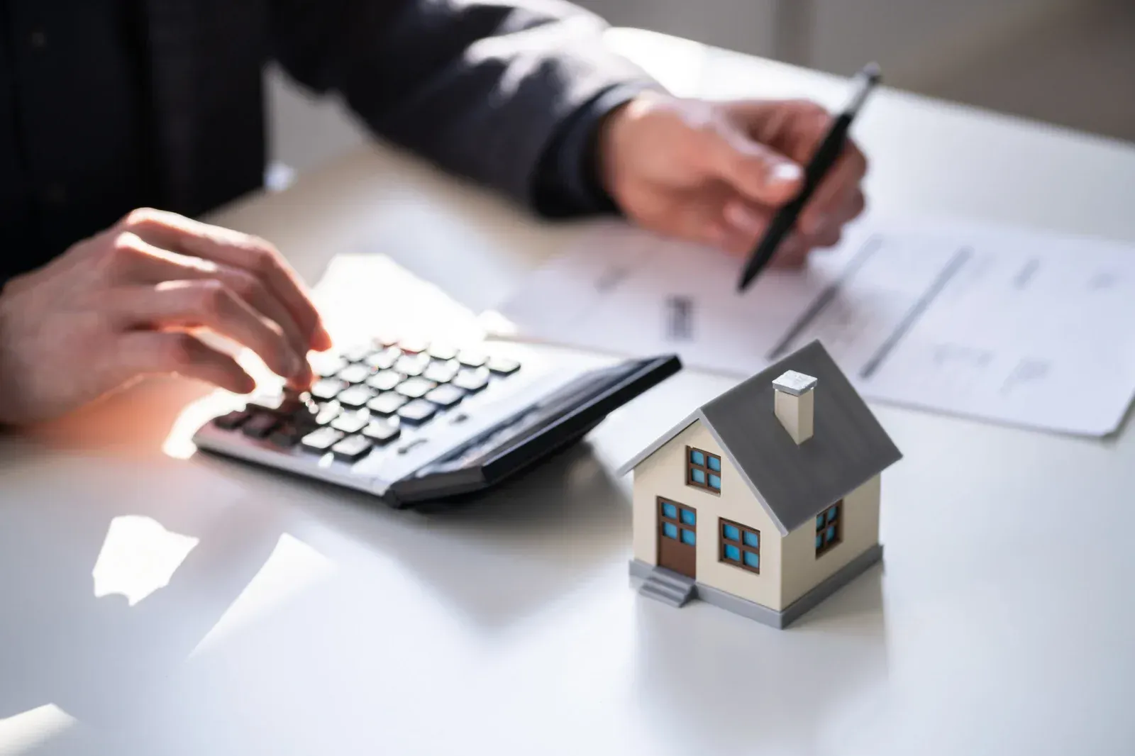 Person calculating expenses for a house model with a calculator and pen.