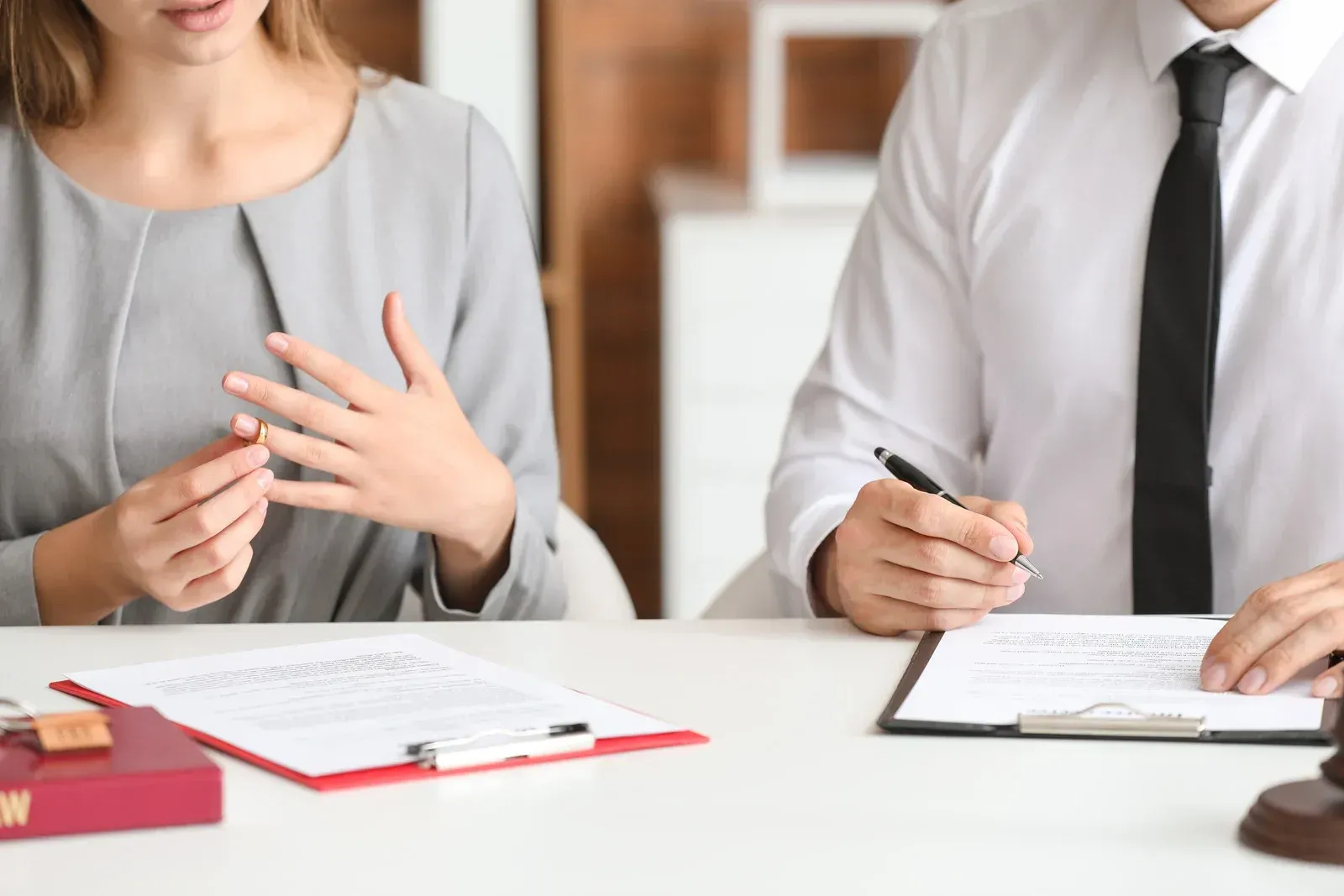 Woman gesturing, discussing documents with a man at a table. Legal setting.