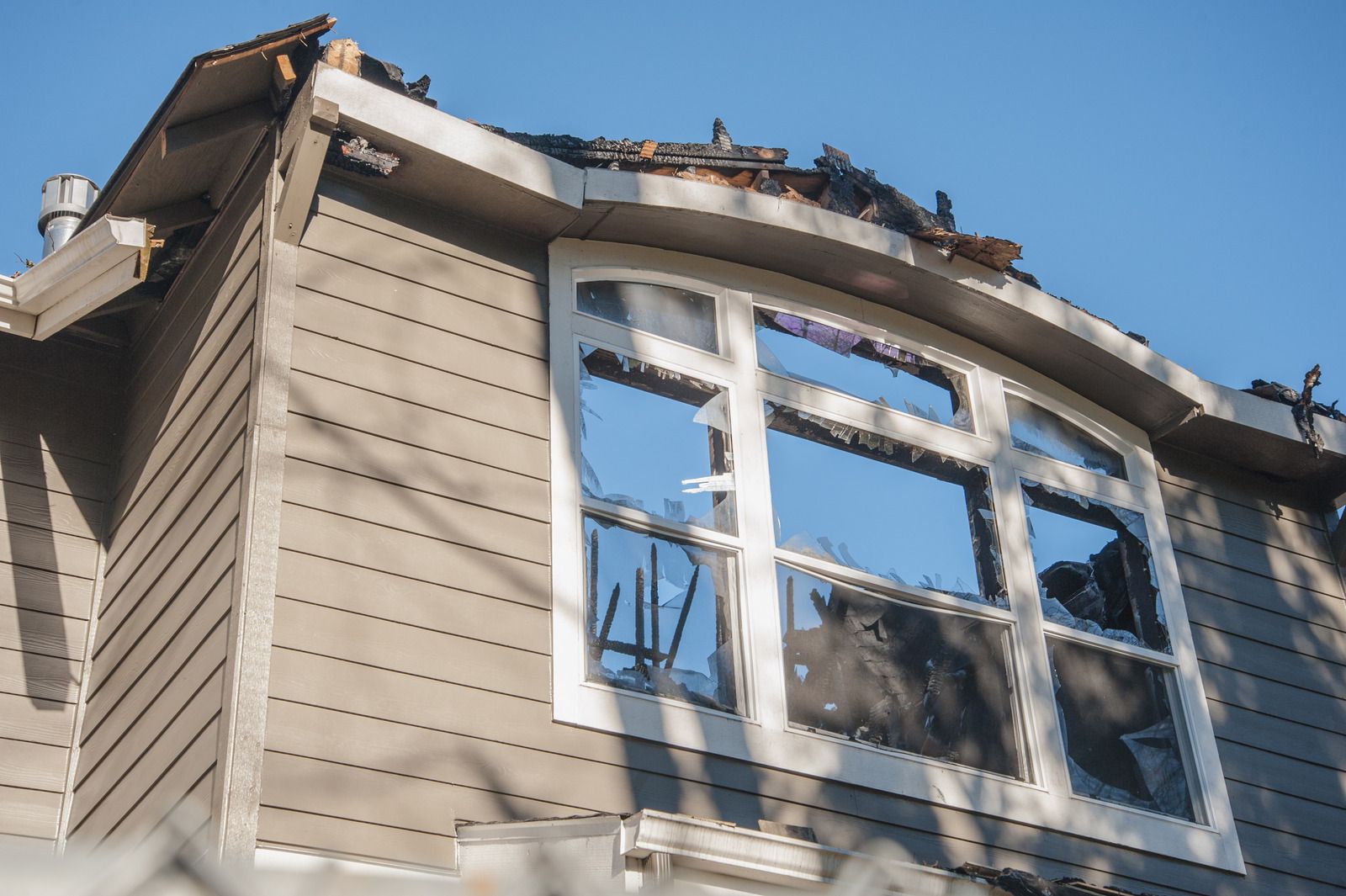 House exterior with fire damage around a window, brown siding, blue sky.