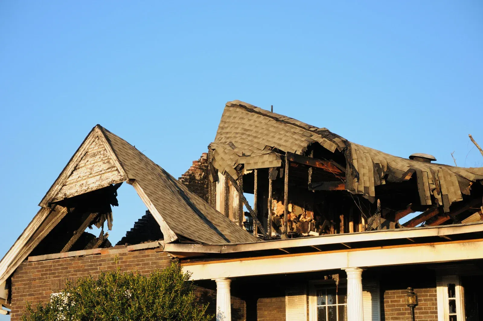 Damaged house roof and frame with clear blue sky.