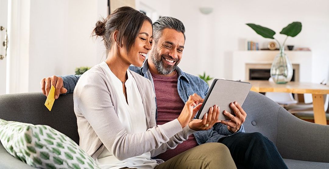 A man and a woman are sitting on a couch looking at a tablet.