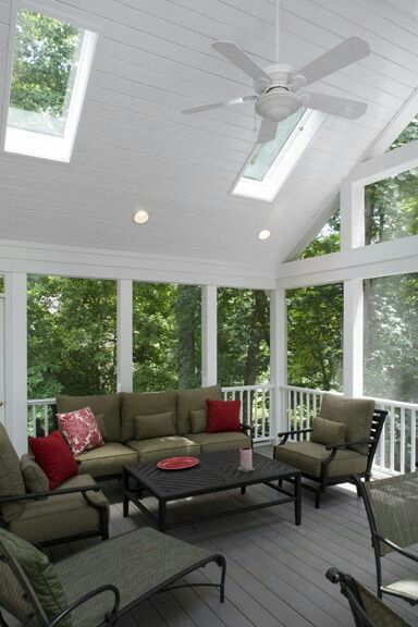Screened-in porch with green sofa, chairs, and coffee table; skylights and ceiling fan; overlooking trees.
