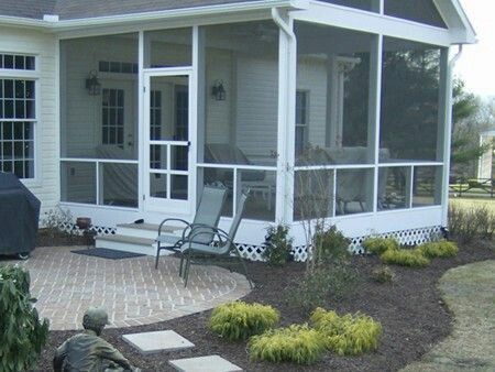 Screened-in porch with white trim, brick patio, and landscaping. A chair sits on the patio.