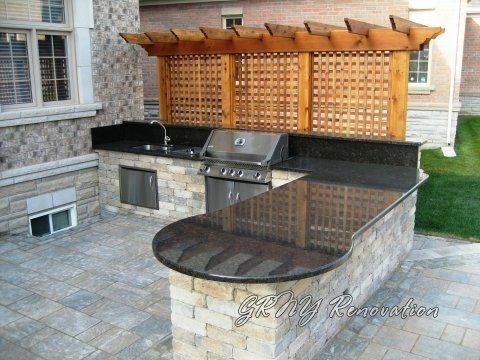 Outdoor kitchen with granite countertop, built-in grill, sink, and wooden pergola.