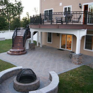 Backyard patio with fire pit, deck, and stairs leading up to house.