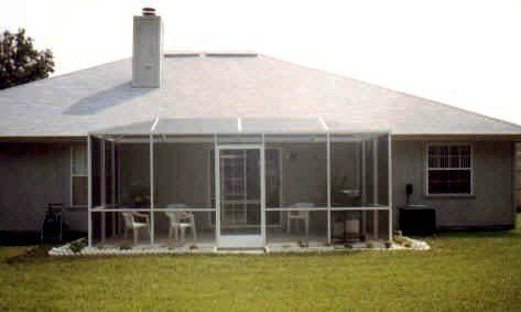 Screened-in porch attached to a house with white framing, door, and chairs. Situated on a grassy lawn.