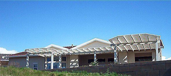 A light-colored house with a pergola and a low stone wall, set against a blue sky.
