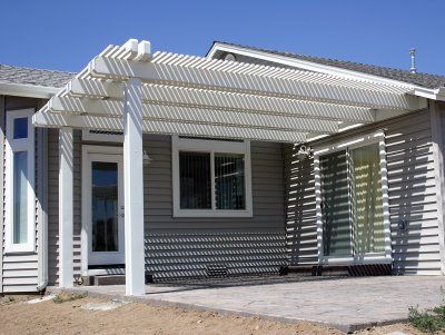 White pergola covering a patio next to a house with gray siding and glass doors/windows.