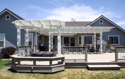 Backyard deck with white pergola, built-in grill, and access to a house with blue siding.