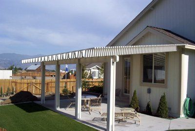 White aluminum patio cover attached to a beige house, over a concrete patio with furniture.