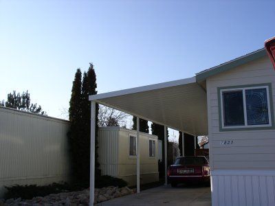 Car parked under a carport attached to a light-colored building with a window. Blue sky.