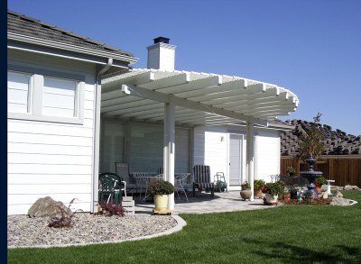 White pergola over a patio next to a house with outdoor furniture and a fountain.