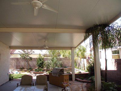 Covered patio with ceiling fans, chairs, grill, and a backyard with trees and a fence.